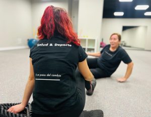 Imagen de un técnico de entrenamiento con la camiseta de FIX que pone el slogan de nuestra clínica sanitaria "A un paso del cambio", guiando un ejercicio personalizado con una paciente