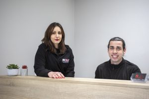 Imagen de los recepcionistas de la clínica sanitaria mientras sonríen y demuestran cómo atienden con empatía y amabilidad en el mostrador de la entrada de FIX.