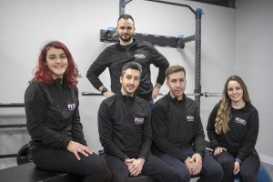 Imagen del equipo de entrenadores posando para la foto oficial de nuestra clínica sonriendo de forma distendida en la sala de entrenamiento.